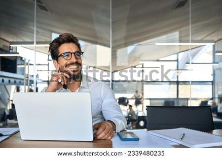 Happy Latin business man working at laptop in office looking away. Happy young businessman professional using computer sitting at desk thinking of corporate technology ai solutions. Copy space
