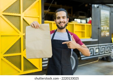 Happy latin chef pointing to a mock-up bag ready for customer delivery from the fast food truck - Powered by Shutterstock