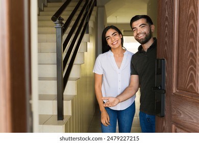 Happy Latin couple welcomes you into their new home, radiating joy and excitement in their modern space - Powered by Shutterstock