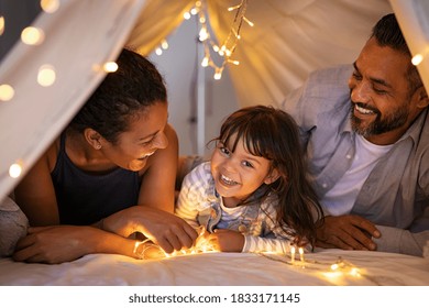 Happy latin daughter with african mom and indian dad playing in kid tent. Little girl talking to mother and father lying on bed in hut. Funny cute girl with multiethnic parent in cozy shelter at home. - Powered by Shutterstock