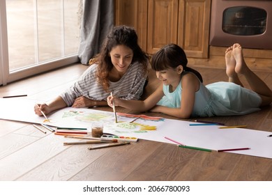 Happy Latin daughter kid and mom painting in water colors, lying on heating parquet floor in kitchen, improving craft art skills, enjoying creative hobby together. Mother teaching kid to draw - Powered by Shutterstock