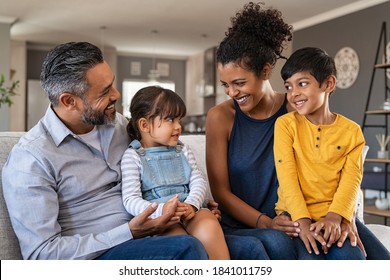 Happy Latin Family Sitting On Sofa And Laughing Together. Middle Eastern Parents Playing With Daughter And Son At Home. Indian Father Sitting With Daughter While African Mother And Brother Smiling.