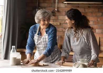 Happy Latin grown up daughter and senior mother cooking in home kitchen together, rolling dough for homemade pastry, bakery food, talking, laughing, enjoying leisure time, common hobby together - Powered by Shutterstock