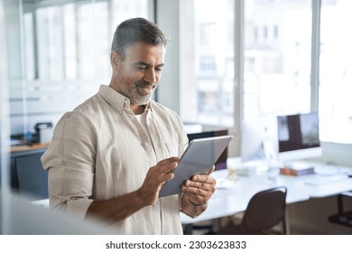 Happy Latin Hispanic bearded stylish mature adult professional business man, smiling Indian senior businessman CEO holding digital tablet using fintech tab application standing inside company office. - Powered by Shutterstock