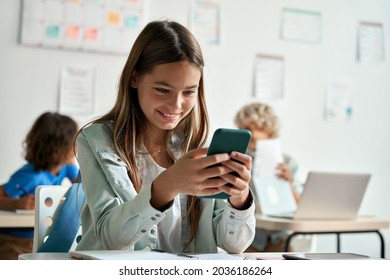 Happy latin hispanic kid girl school student using smartphone in classroom. Preteen child holding mobile cell phone having fun with apps playing games and checking social media at school during break. - Powered by Shutterstock