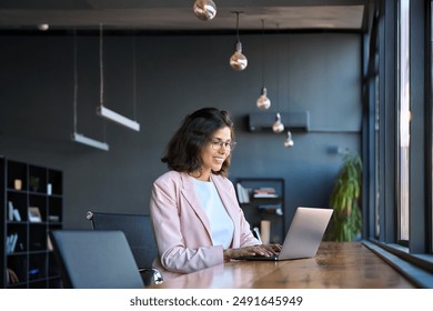 Happy latin hispanic young business woman working on laptop computer in company office. Smiling Indian entrepreneur manager businesswoman using pc for communication, learning at workplace. Copy space