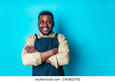 Happy Latin Man In Cotton Shirt Ant Black Apron In Blue Studio Looking At Camera And Feeling Good