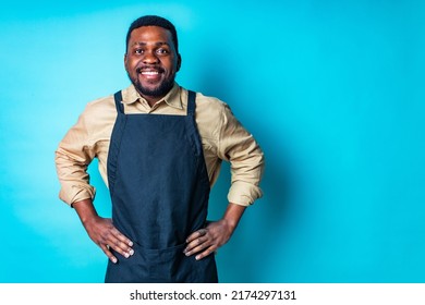 Happy Latin Man In Cotton Shirt Ant Black Apron In Blue Studio Looking At Camera And Feeling Good