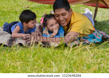 Happy latin man with his two little children having fun in the hovel made of clothing. Relaxing in the countryside.