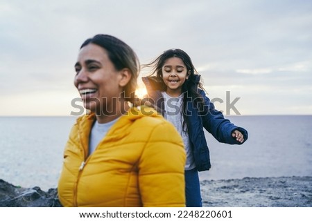 Happy latin mother and daughter having fun together on the beach during winter time - Focus on girl face
