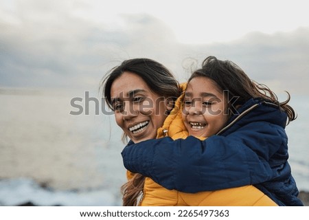Happy latin mother and daughter having fun on the beach during winter time - Mom and child outdoor