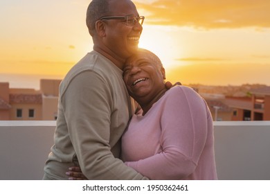 Happy Latin senior couple having romantic moment embracing on rooftop during sunset time - Elderly people love concept 