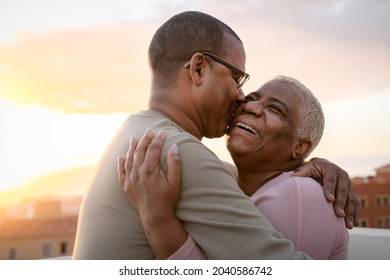 Happy Latin senior couple having romantic moment embracing on rooftop during sunset time - Elderly people love concept 