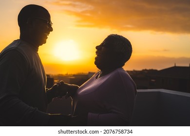 Happy Latin Senior Couple Having Romantic Moment Dancing On Rooftop During Sunset Time