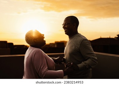 Happy Latin senior couple having romantic moment on rooftop during sunset time - Elderly people love concept - Powered by Shutterstock