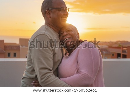 Happy Latin senior couple having romantic moment embracing on rooftop during sunset time - Elderly people love concept 