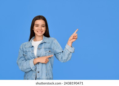 Happy Latin teen girl pointing aside standing on blue background. Smiling pretty freckled gen z brunette Hispanic teen student wearing denim outfit looking at camera presenting product or service ad. - Powered by Shutterstock