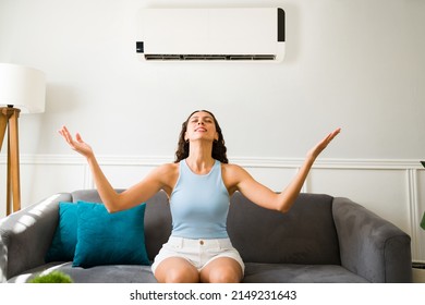 Happy Latin Woman Enjoying The Cold Air Flow Of Her Air Conditioner During A Hot Summer At Home 