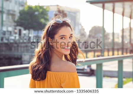 Happy latin woman looking behind while walking on street. Beautiful young woman enjoying vacation during summer. Cheerful girl in smart casual walking and looking at camera while smiling.
