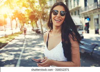 Happy Latin Woman In Summer Sun Glasses Smiling Brightly While Holding Smart Phone Strolling Outdoors In The City At Sunny Day,female Person Using Mobile Standing With Composition Copy Space On A Side