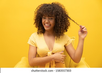 Happy laughing American African woman with her curly hair on yellow background. Laughing curly woman in sweater touching her hair and looking at the camera.