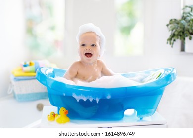 Happy Laughing Baby Taking A Bath Playing With Foam Bubbles. Little Child In A Bathtub. Smiling Kid In Bathroom With Colorful Toy Duck. Infant Washing And Bathing. Hygiene And Care For Young Children.