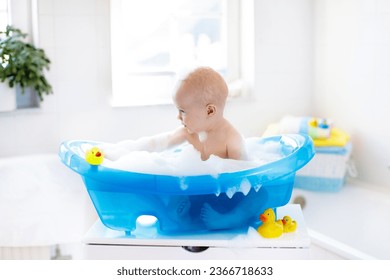 Happy laughing baby taking a bath playing with foam bubbles. Little child in a bathtub. Smiling kid in bathroom with colorful toy duck. Infant washing and bathing. Hygiene and care for young children. - Shutterstock ID 2366718633