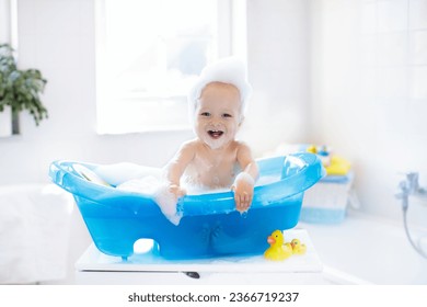 Happy laughing baby taking a bath playing with foam bubbles. Little child in a bathtub. Smiling kid in bathroom with colorful toy duck. Infant washing and bathing. Hygiene and care for young children. - Shutterstock ID 2366719237