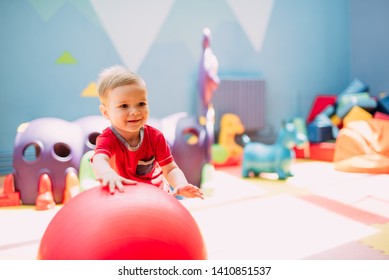Happy laughing boy 1-2 years old having fun in ball pit on birthday party in kids amusement park and indoor play center. Child playing with colorful balls in playground ball pool. 