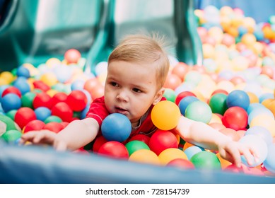 Happy Laughing Boy 1-2 Years Old Having Fun In Ball Pit In Kids Amusement Park And Indoor Play Center. Child Playing With Colorful Balls In Playground Ball Pool. Activity Toys For Little Kid.