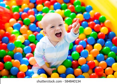Happy laughing boy having fun in ball pit on birthday party in kids amusement park and indoor play center. Child playing with colorful balls in playground ball pool. Activity toys for little kid.