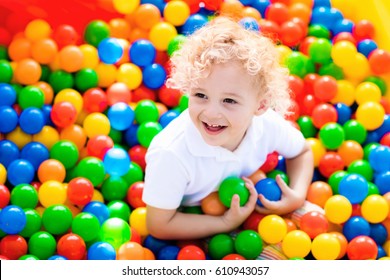 Happy Laughing Boy Having Fun In Ball Pit On Birthday Party In Kids Amusement Park And Indoor Play Center. Child Playing With Colorful Balls In Playground Ball Pool. Activity Toys For Little Kid