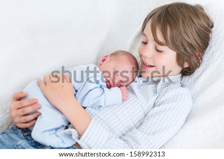 Happy laughing boy holding his sleeping newborn baby brother