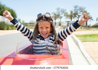 Happy laughing boy raising hand in victory after riding gokart outdoor. KId having fun and driving toy race car on street. Child exult while riding an electric or peddle toy auto wearing pilot helmet.