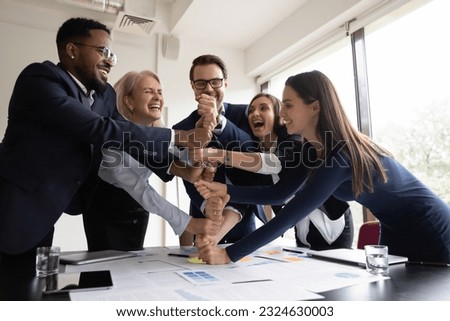 Happy laughing businesspeople colleagues of different age and race stacking fists on meeting or motivation training in office demonstrating togetherness, unity, cooperation and corporate team spirit