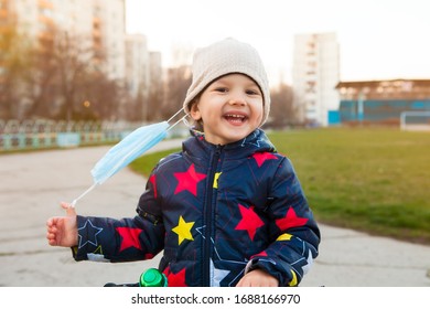 happy and laughing child on a walk in a city park removes a medical mask from his face. Walking on a street without a mask during the quarantine. End of quarantine - Powered by Shutterstock