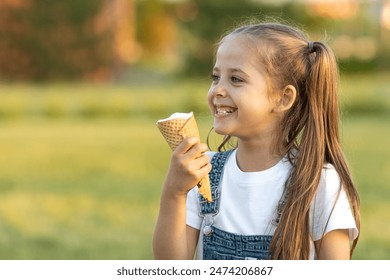 A happy laughing child in summer clothes eats ice cream on a hot day in park. Ice cream in a waffle cone. A happy and contented child at summer. - Powered by Shutterstock