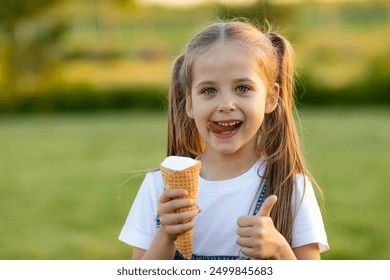 A happy laughing child in summer clothes eats ice cream on a hot day in park. Ice cream in a waffle cone. A happy and contented child at summer. - Powered by Shutterstock