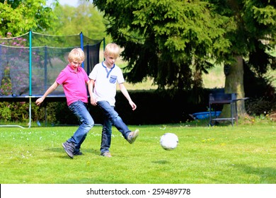 Happy Laughing Children, Twin Teenage Boys, Playing Soccer In The Garden At The Backyard Of The House On Sunny Summer Vacation Day