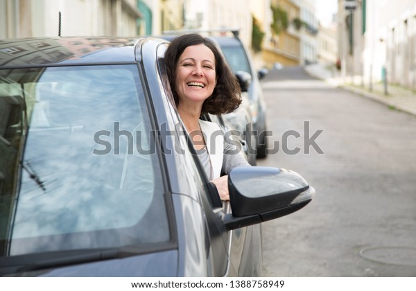 Happy laughing customer excited with new car.\
Overjoyed young woman hanging out of car side window and smiling at\
camera. New car concept