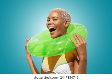 Happy laughing fun young woman holding green swim ring, African latin American woman isolated on blue background. Concept of a seaside vacation, shopping for a summer beach holiday or travel - Powered by Shutterstock