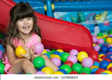 Happy Laughing Girl Kid Having Fun At Indoor Play Center. Child Playing With Colorful Balls In Playground Ball Pool. Holiday