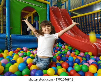 Happy laughing girl kid having fun at indoor play center. Child playing with color balls in playground ball pool. Holiday