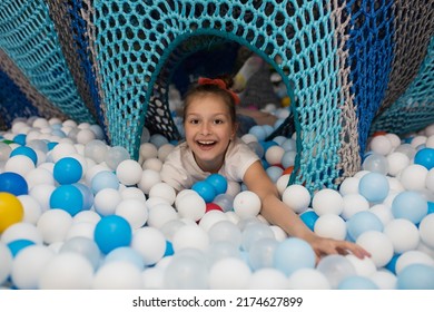 Happy Laughing Girl Playing With Toys, Colorful Balls On The Playground, In A Dry Pool. Little Cute Kid Having Fun In Balloon Pit At Birthday Party At Kids Amusement Park And Indoor Play Center