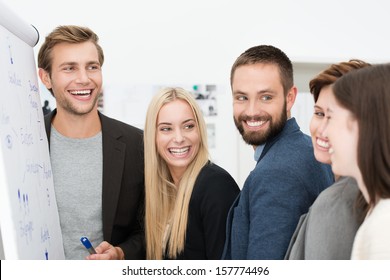 Happy Laughing Group Of Diverse Young Professional Businesspeople Standing Together In Front Of A Flip Chart During A Meeting Or Presentation