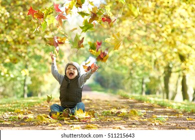 Happy Laughing Kid Throwing Autumn Fall Leaves In An Autumn Alley                              