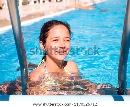 Happy laughing little girl playing in outdoor swimming pool on a hot summer day. A girl in colorful bathing suit learning to swim in tropical resort. Water fun for children