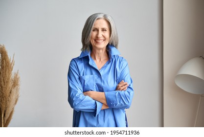 Happy Laughing Mature Elder 60s Business Woman Standing Indoors. Senior Mid Age Older Stylish Look Woman Portrait With Crossed Arms Looking At Camera At Modern Home Office.