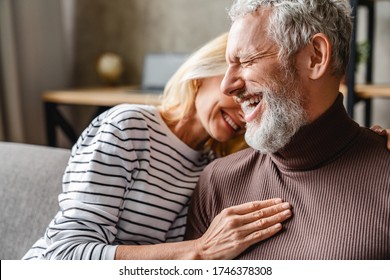 Happy Laughing Middle Aged Couple Bonding While Relaxing Sitting On Sofa