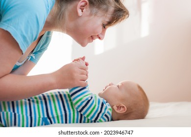 Happy Laughing Mom And Daughter Lie On Their Backs. Happy Smiling Mother And Baby Lying On Bed At Home. Side View.